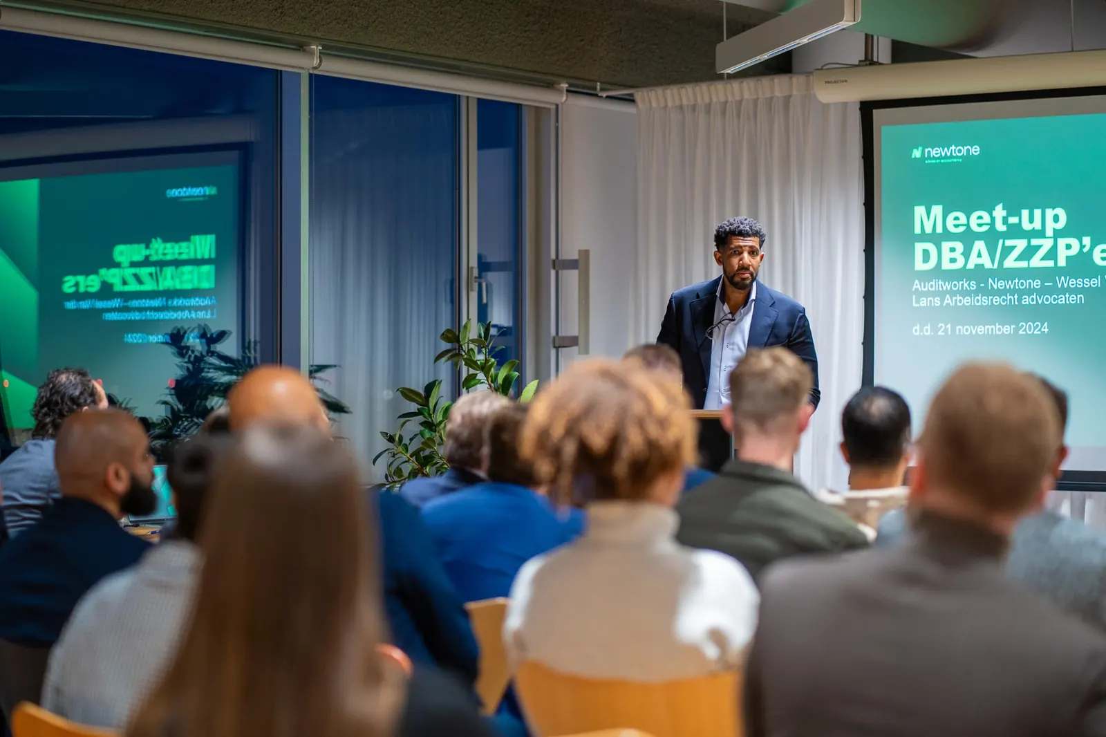 Spreker in pak aan het woord tijdens de Meet-up DBA/ZZP'ers, met het publiek op de voorgrond